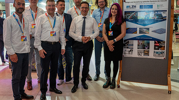 Seven men and one women stand in a half-circle next to a poster in the aufhof.